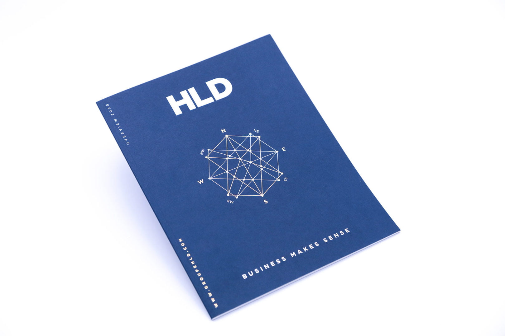 Un livret bleu avec HLD en grandes lettres blanches en haut, un dessin géométrique de compas au centre et le texte BUSINESS MAKES SENSE en bas. Le livret est placé sur un fond blanc.