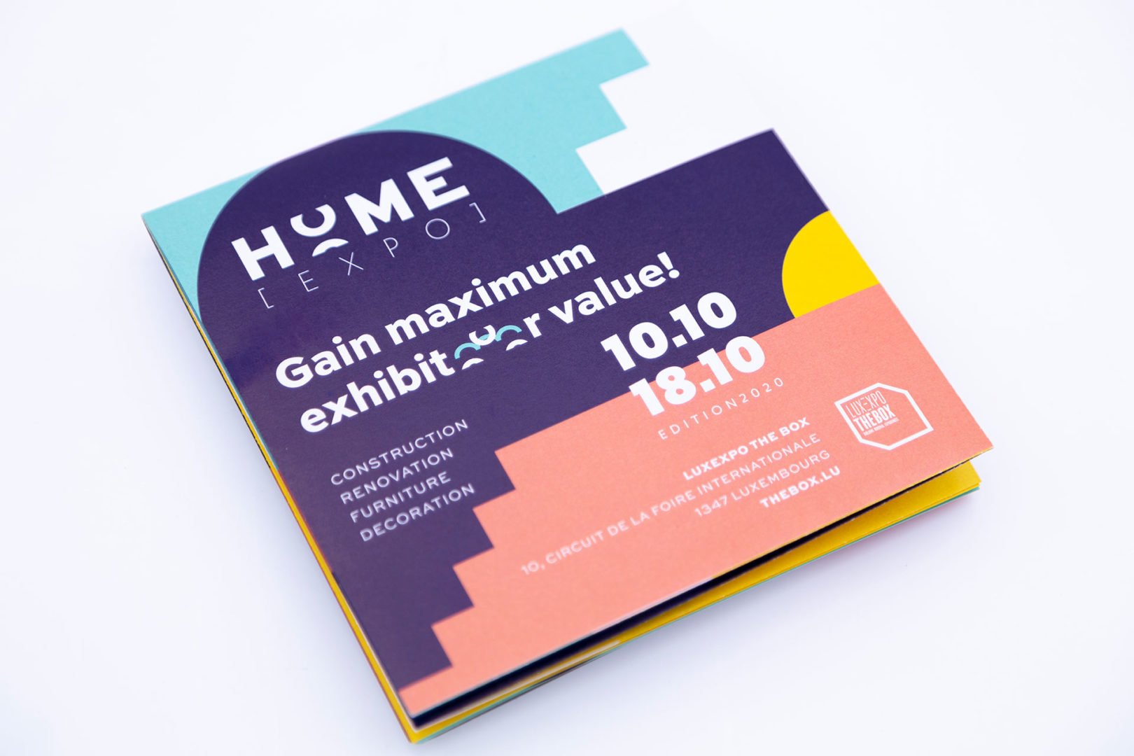 Un flyer plié en couleurs pour la promotion de HOME EXPO avec le slogan Gain maximum de valeur pour l'exposant ! et les détails de l'événement : Du 10.10 au 18.10, 2020, au Luxembourg, à Luxexpo The Box. Le design présente des formes géométriques.