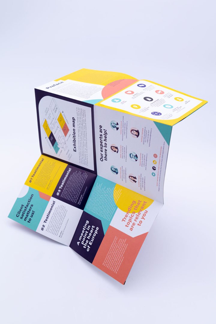 Une brochure colorée, pliée en plusieurs panneaux, comportant du texte, des diagrammes, des icônes et des photos de personnes, affichés debout sur un fond blanc. Le design utilise des sections jaunes, sarcelles, noires, orange et blanches.