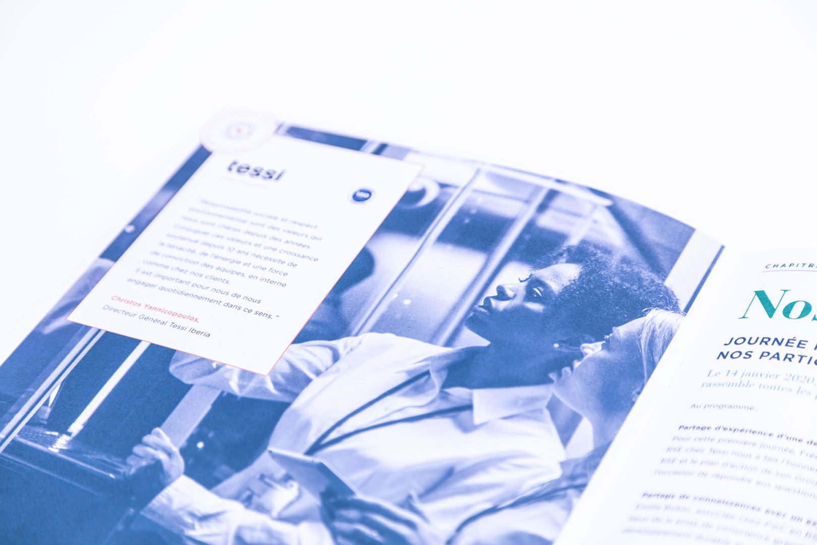 Un magazine est ouvert, affichant une photo teintée de bleu d'une personne en blouse de laboratoire examinant un panneau de verre. Des zones de texte et une écriture en français sont visibles sur la page. Le fond est blanc.