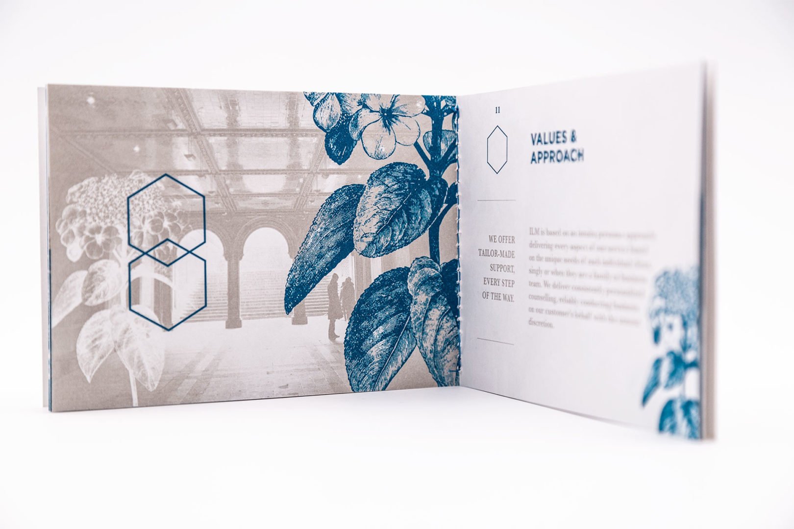 Un livret ouvert présente une photo sépia d'un couloir orné avec des illustrations botaniques bleues et des formes géométriques en surimpression, ainsi que les titres VALUES & APPROACH sur la page de droite.