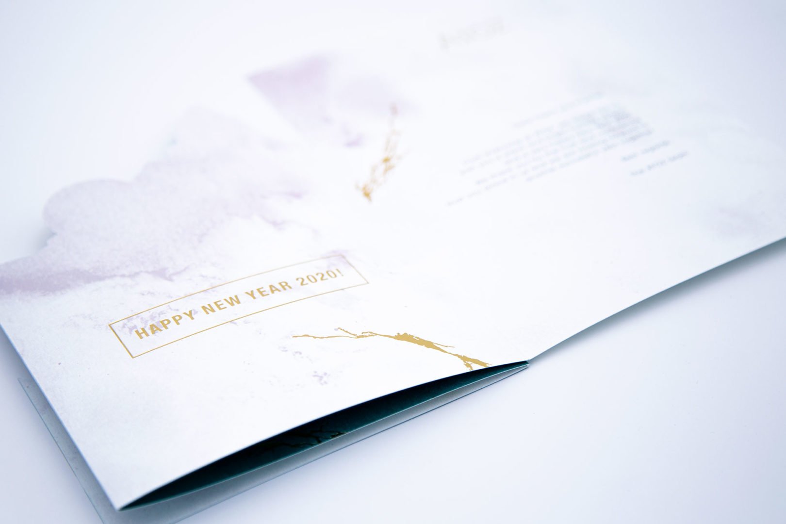 Gros plan sur une carte de vœux ouverte au design minimaliste blanc et or. La carte affiche le texte