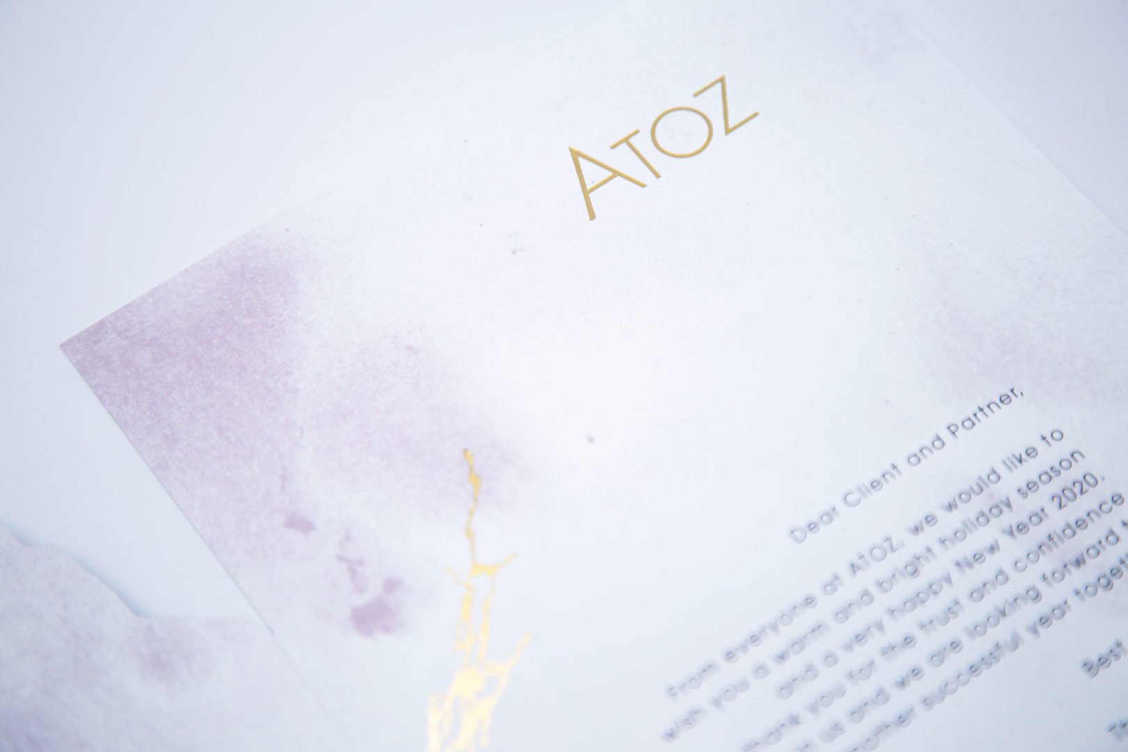 Gros plan d'une lettre portant l'en-tête ATOZ en texte doré sur un fond blanc et violet clair. La lettre semble formelle, adressée à un client ou à un partenaire. Une partie du texte est visible, mais la plus grande partie est floue.