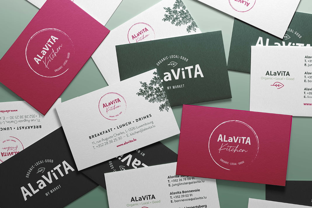 Assortiment dispersé de cartes de visite de couleur bordeaux, blanche et verte, représentant la marque ALaViTA Kitchen avec différents styles de logo et des informations de contact, présentées sur une surface vert clair.