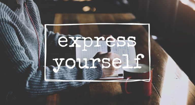 Une personne vêtue d'un pull gris écrit dans un carnet à une table en bois, avec une tasse rouge à proximité. Les mots "express yourself" (exprimez-vous) sont inscrits en caractères gras et blancs dans un cadre rectangulaire.