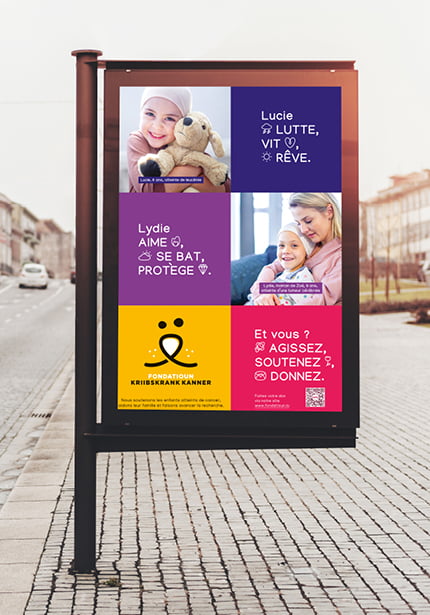 Une plaque de rue comporte quatre panneaux colorés représentant des enfants et un adulte souriants. Le texte encourage le soutien à une fondation pour l'enfance, avec un code QR et le logo de la Fondation Kriibskrank Kanner.