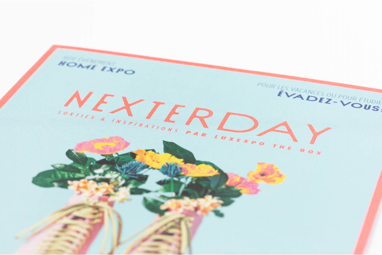 Gros plan sur la couverture d'un magazine lifestyle intitulé NEXTERDAY : Sorties & Inspirations par Luxexpo The Box, avec des photos de fleurs dans des vases et des accents bleu clair et corail, soulignant les tendances et les événements au Luxembourg.