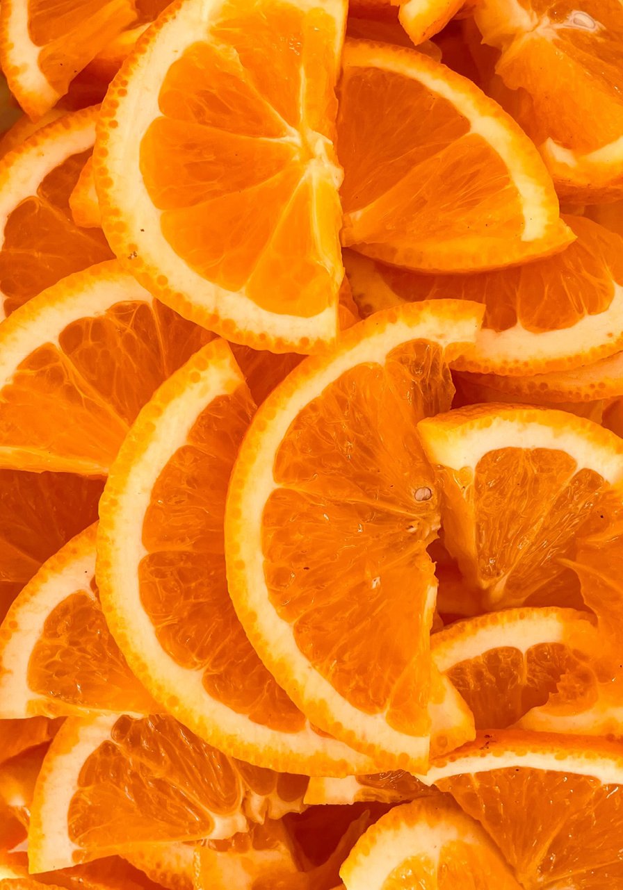Gros plan de plusieurs tranches d'orange se chevauchant, montrant leur couleur orange vif et leur texture juteuse avec des écorces et des segments visibles.