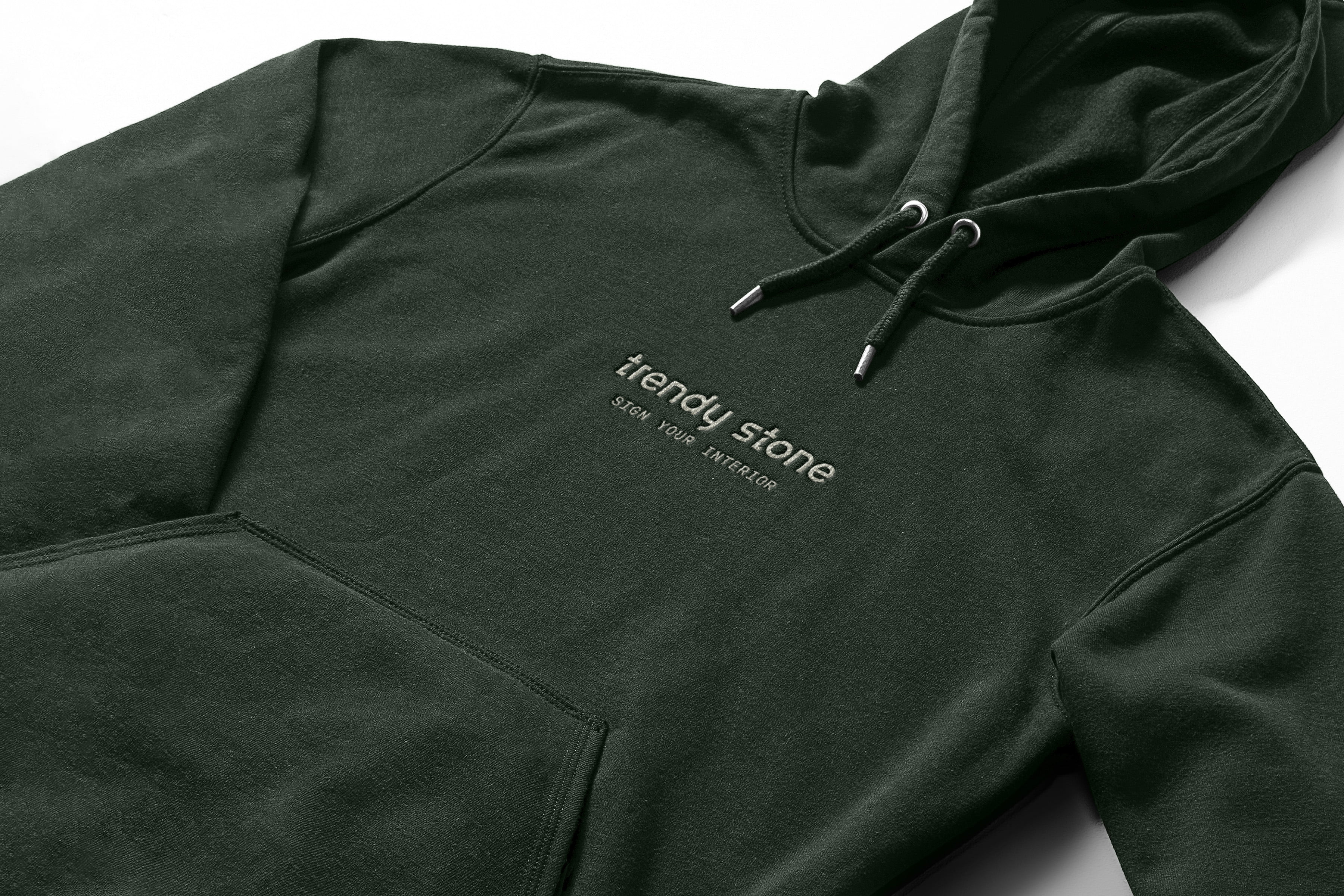 Un sweat à capuche vert foncé avec le logo de Trendy Stone et SHOW YOUR ATTITUDE imprimé en blanc sur le devant, avec une poche avant et des cordons de serrage. Le sweat à capuche est posé à plat sur un fond blanc.