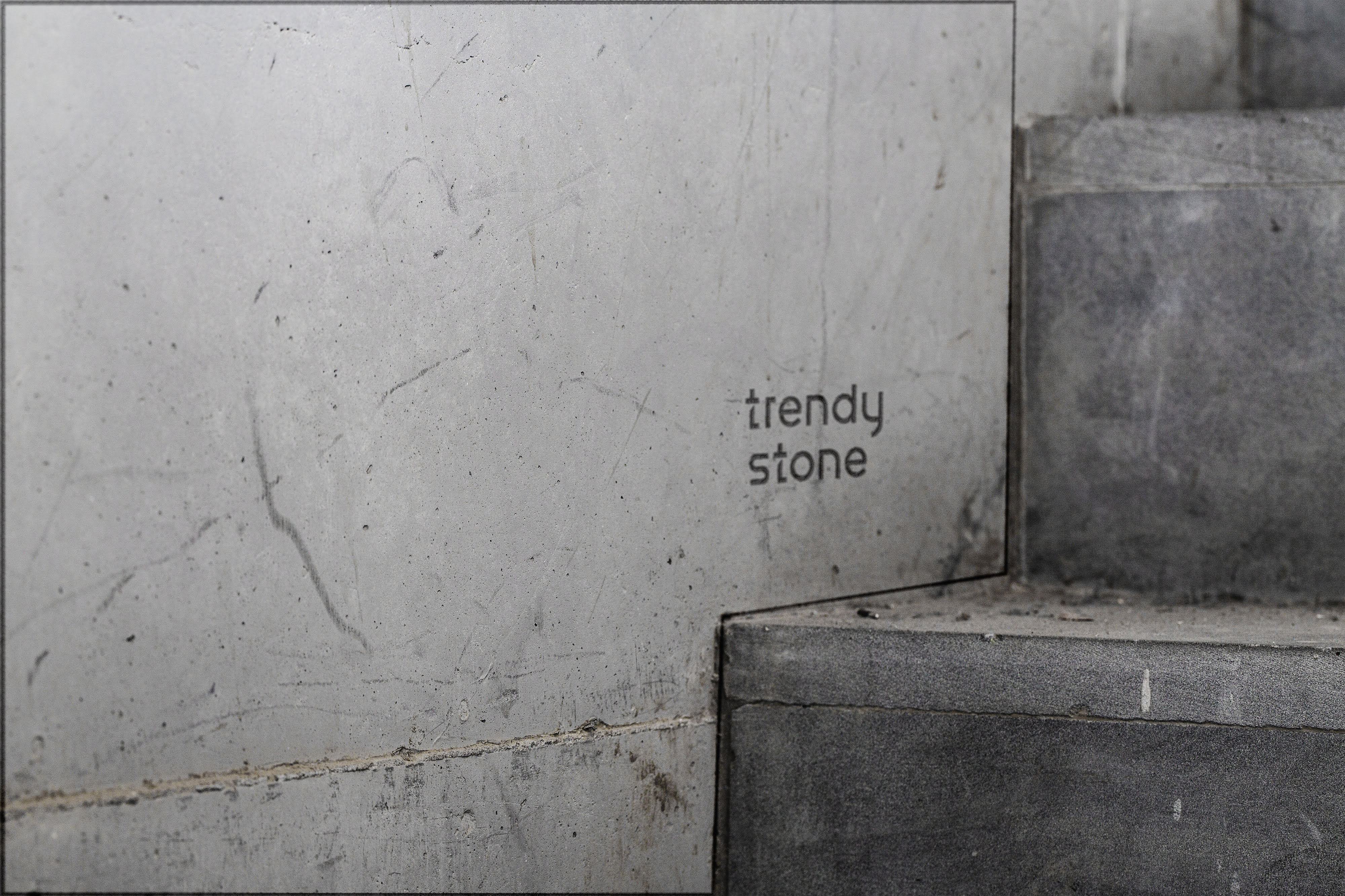 Gros plan sur un escalier en béton à côté d'un mur gris clair, légèrement taché, avec le logo "Trendy Stone" dans une petite police simple sur le mur près de l'escalier, faisant allusion à leur nouvelle présence sur le web.