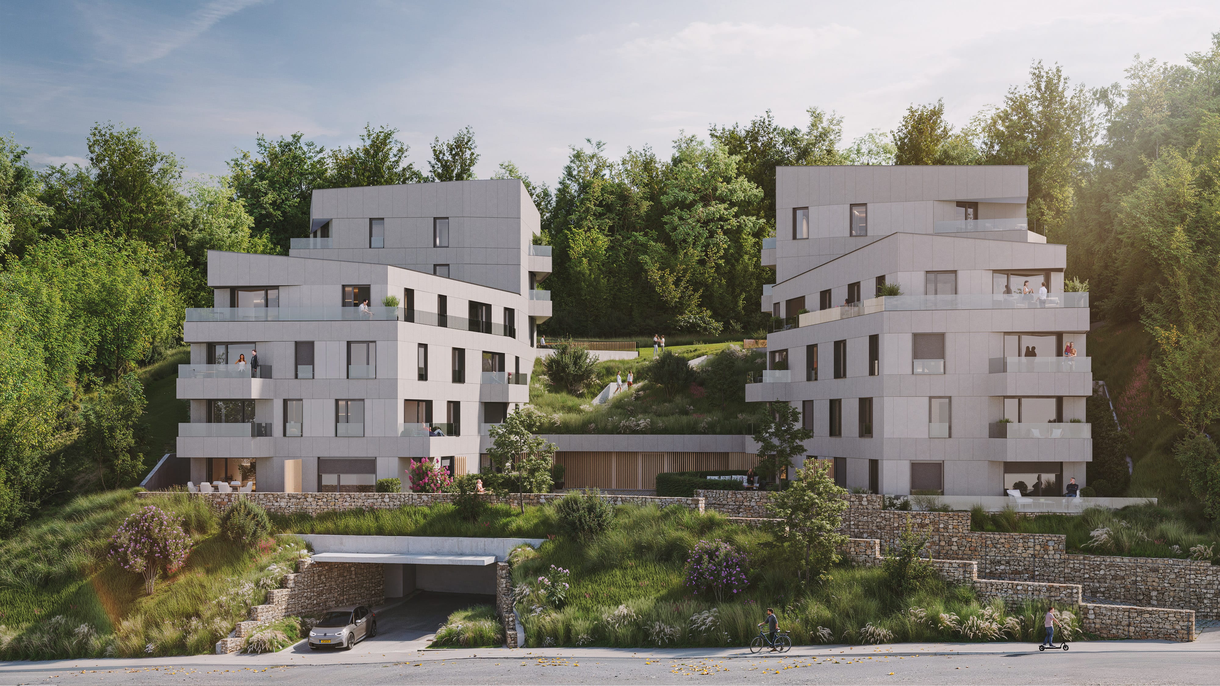 Deux immeubles d'habitation modernes, à plusieurs étages, avec de grandes fenêtres et des balcons, situés sur une colline verdoyante avec des arbres en arrière-plan. Une voiture pénètre dans un tunnel en contrebas, et des personnes marchent sur des sentiers entre les bâtiments.