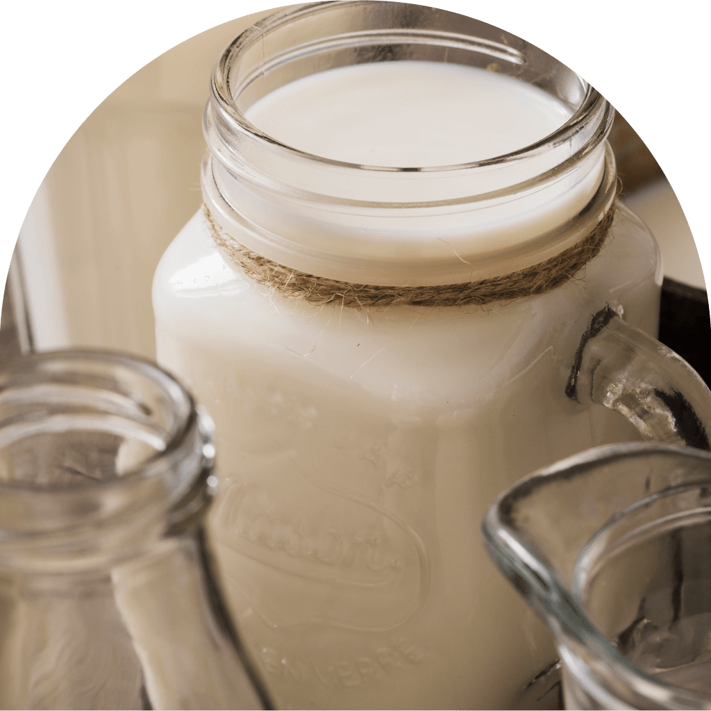 Gros plan sur un pot en verre rempli de lait, décoré d'un nœud en ficelle autour du cou. Des bouteilles en verre vides sont placées au premier plan.