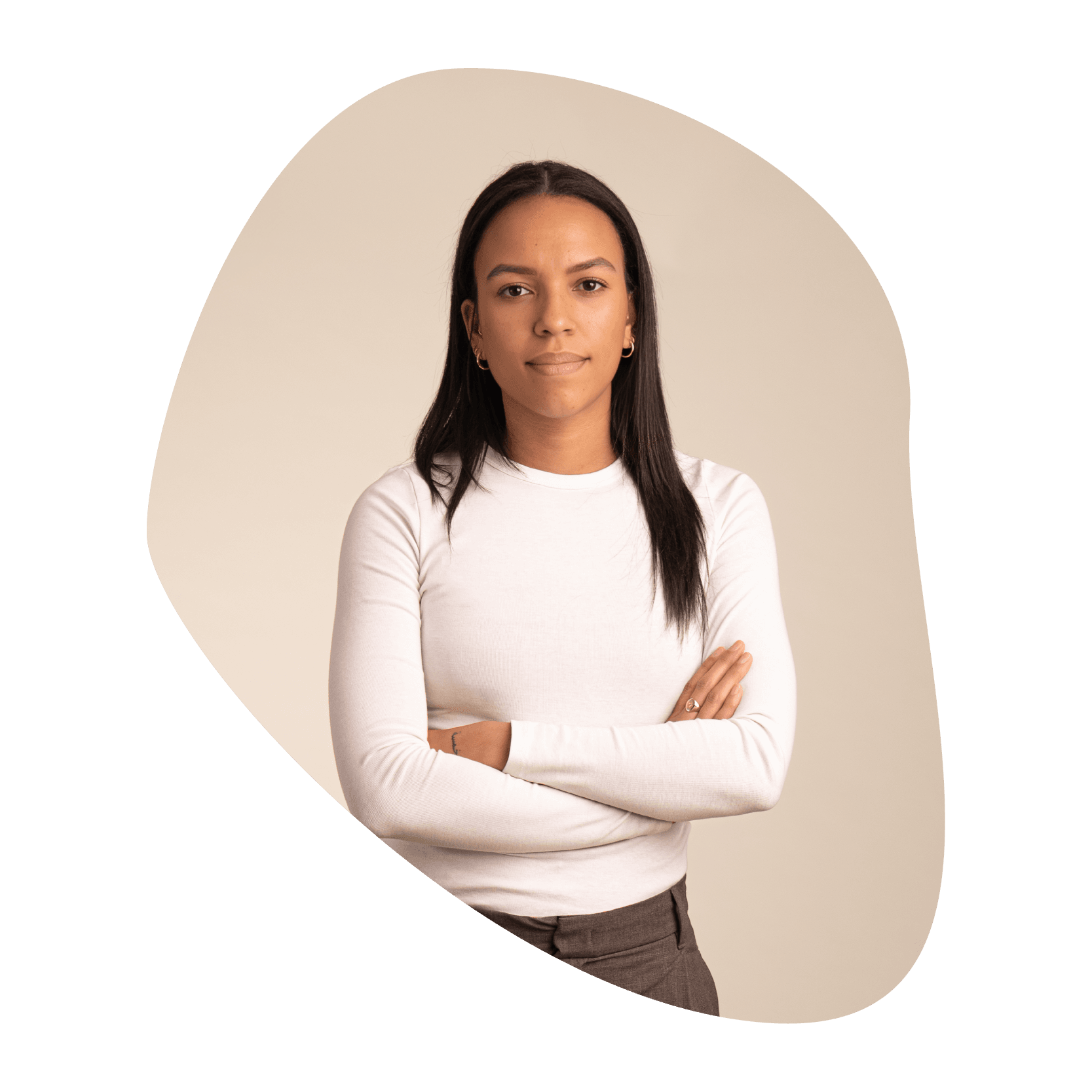 Une femme aux longs cheveux noirs, vêtue d'un haut blanc à manches longues et d'un pantalon marron, se tient debout, les bras croisés, sur un fond beige neutre à la forme abstraite.