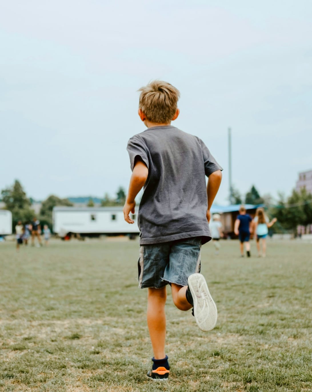 Jeune garçon vu de dos courant dans un champ, en direction d'autres enfants au loin.