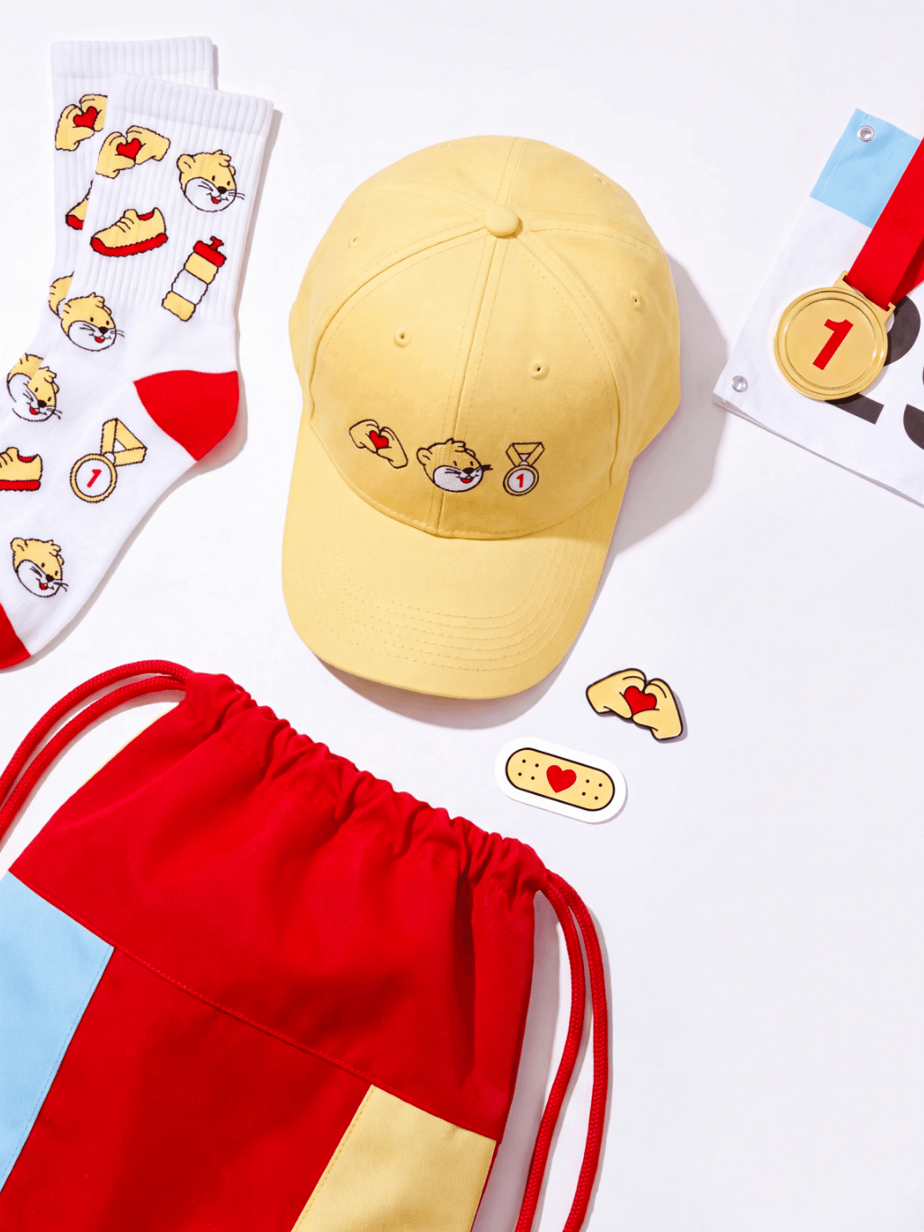 Une casquette jaune ornée de pin's représentant des personnages de dessins animés, des chaussettes blanches aux motifs assortis, un sac à cordon rouge, jaune et bleu, une médaille d'or, ainsi que deux petits pin's en forme de pansement et de bras fléchi avec un cœur.